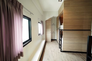 Un pasillo con suelo de madera, una ventana con cortinas y un armario de madera.