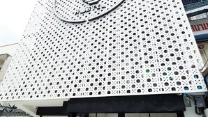 A building with a perforated facade and a large circular logo. - T Hostel at Victory Monument (Bangkok)