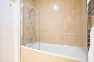 Un baño moderno con ducha de vidrio, bañera blanca y paredes cubiertas de azulejos color beige.