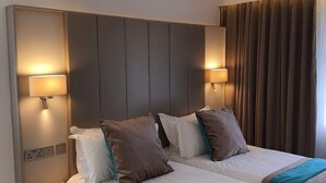 Hotelkamer met twee bedden, elk met hoofdeinde, bedlampjes en een bruine accentmuur.