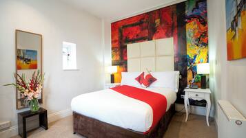 Een hotelkamer met een groot bed, een nachtkastje, een spiegel en een levendig abstract schilderij aan de muur.
