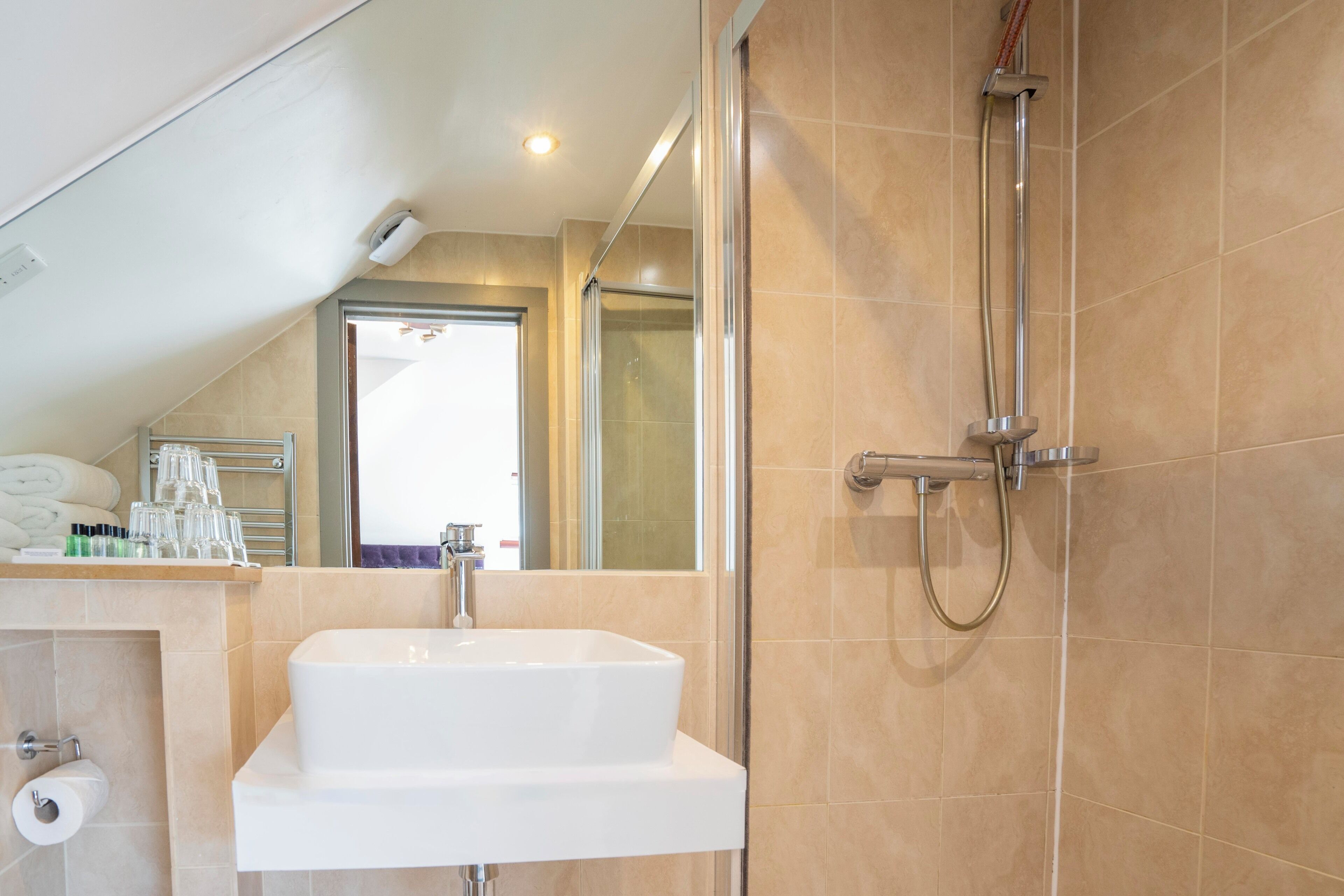 A modern bathroom with a white sink, a glass shower enclosure, and beige tiled walls.