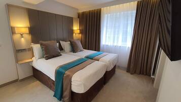 A hotel room with two beds, a large headboard, bedside lamps, and a window with curtains.