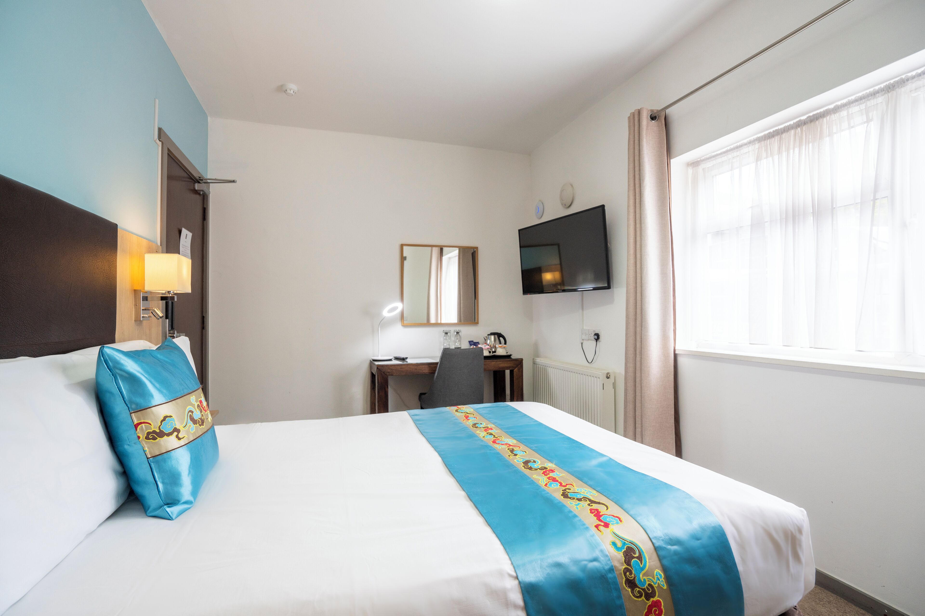 A hotel room with a bed, a desk, a chair, a television, and a window with curtains.