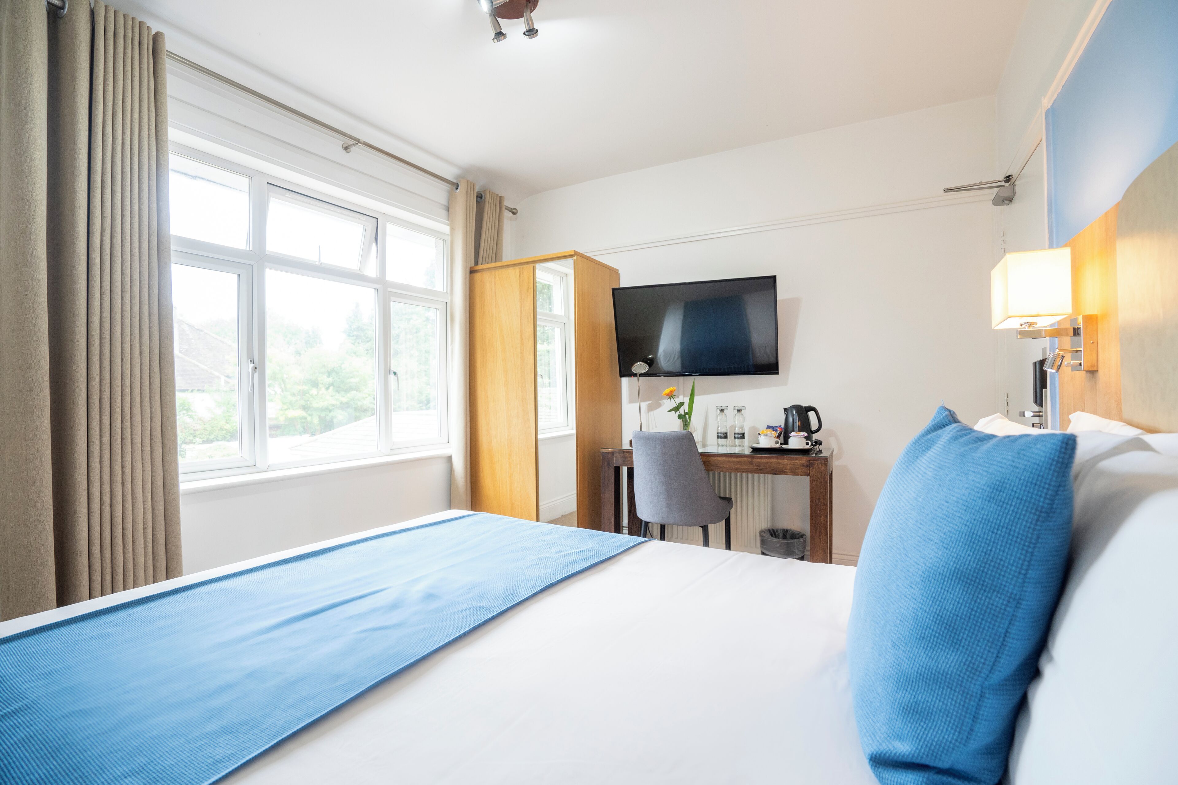 A hotel room with a bed, a desk with a chair, a television, and a window with curtains.