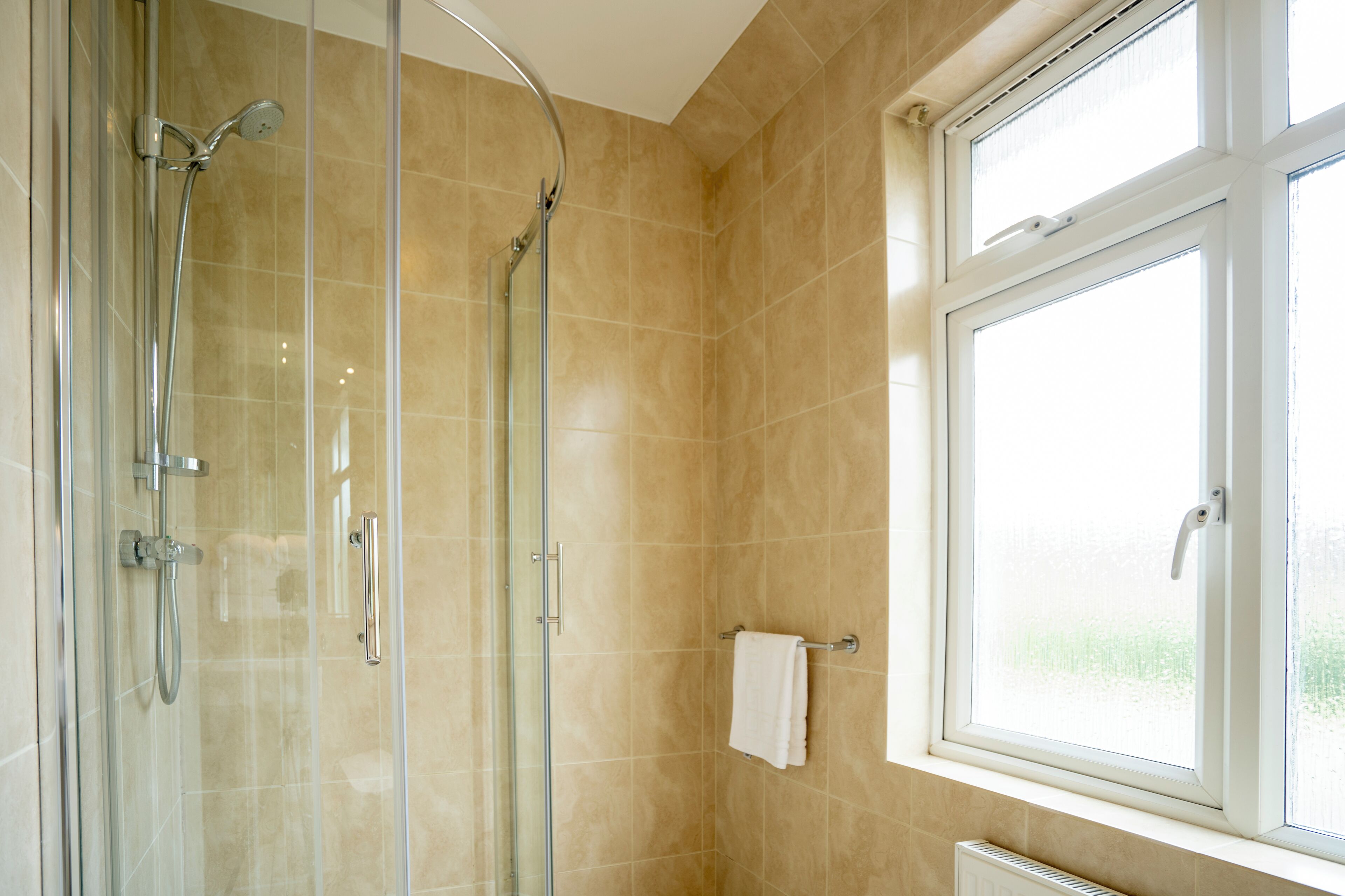 A modern bathroom with a glass shower enclosure, a white towel hanging on a rack, and a window providing natural light.