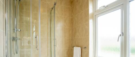 A modern bathroom with a glass shower enclosure, a white towel hanging on a rack, and a window providing natural light.