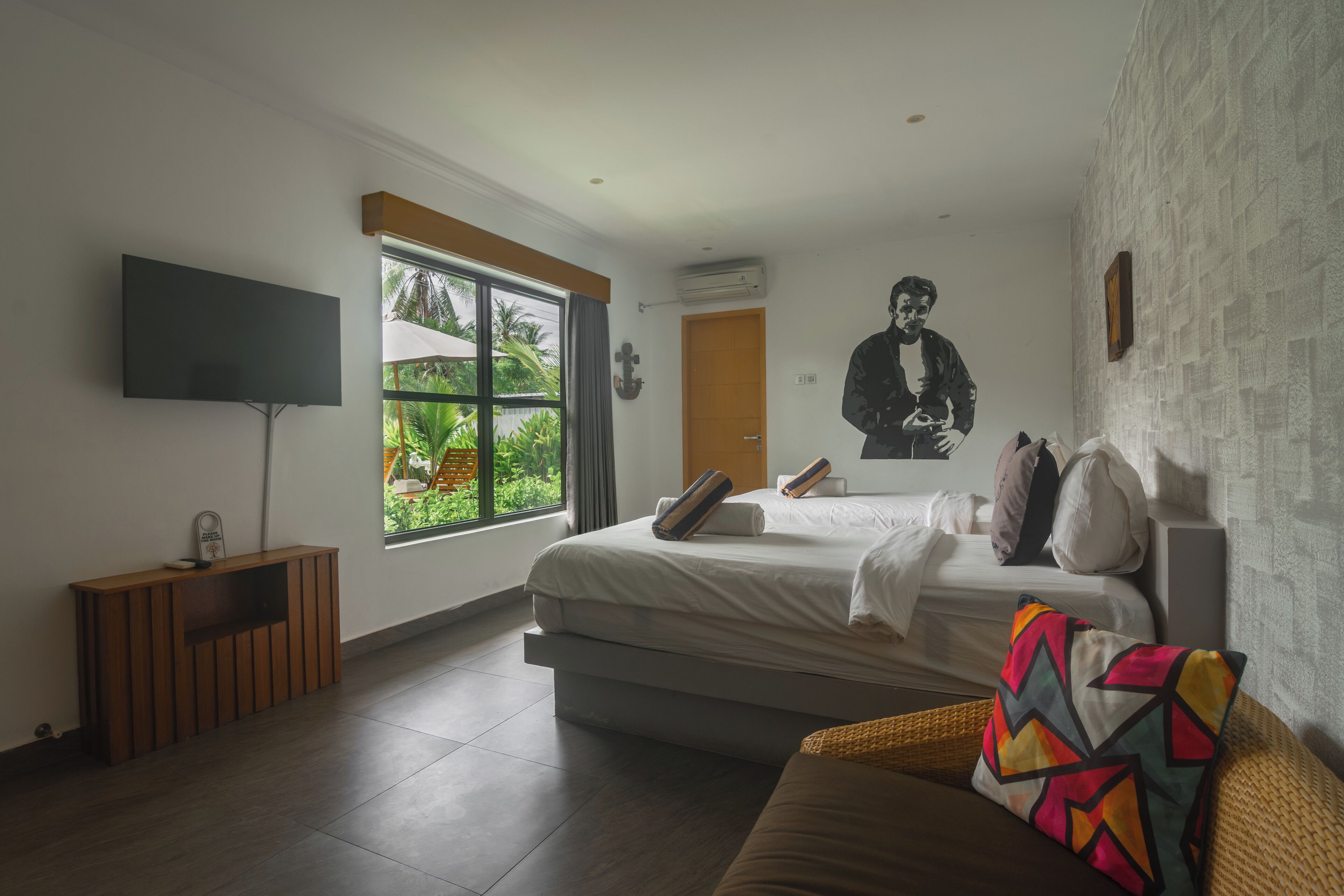 Une chambre moderne équipée d’un lit, d’une télévision, d’une fenêtre donnant sur un espace verdoyant et d’un climatiseur fixé au mur.