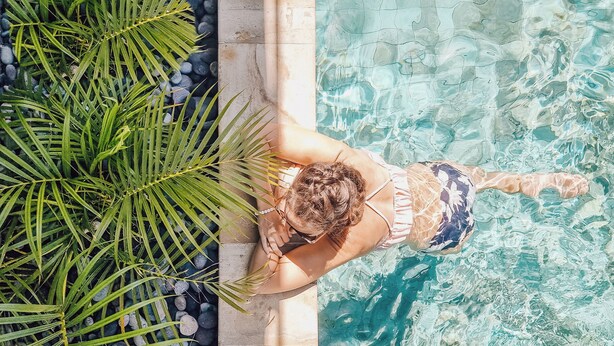 A person swimming in a pool with clear water, surrounded by greenery and a stone border.