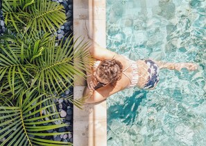 A person swimming in a pool with clear water, surrounded by greenery and a stone border. - Gili Khayangan Villas (Gili Trawangan)