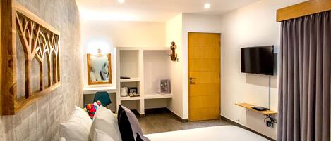 A modern hotel room with a large bed, a television, a wooden door, and a wall-mounted shelf.
