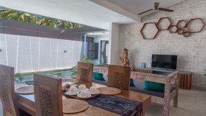 A modern dining area with a pool view, wooden furniture, and a TV.