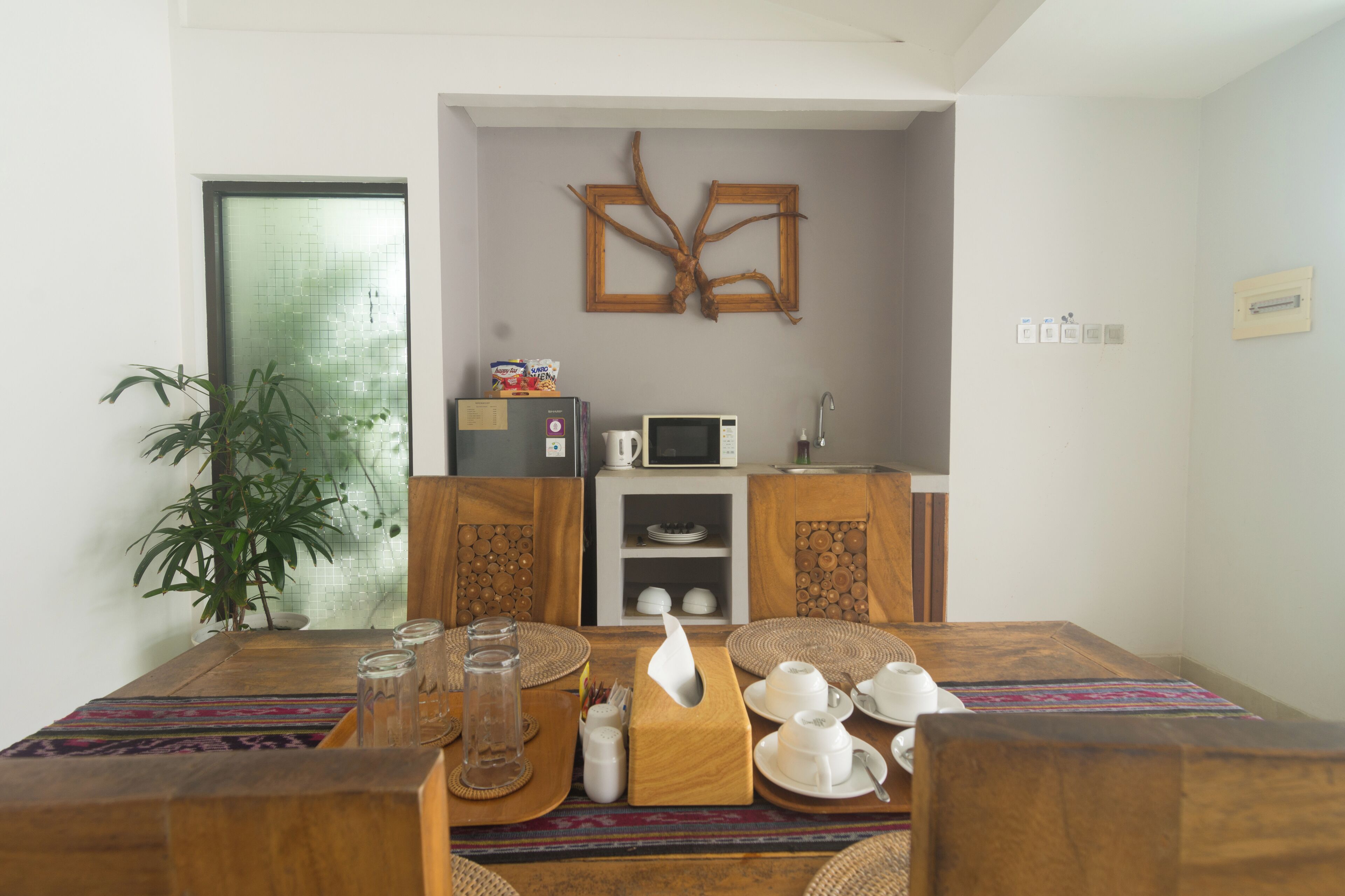 A dining area with a wooden table set for four, a microwave, and a refrigerator in the background.