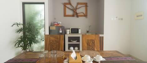 A dining area with a wooden table set for four, a microwave, and a refrigerator in the background.