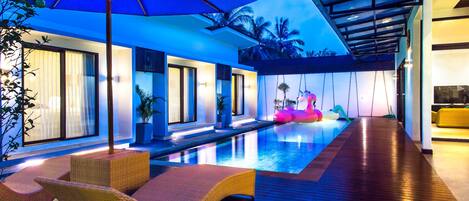 A modern indoor pool area with lounge chairs, a blue umbrella, and a wooden deck.