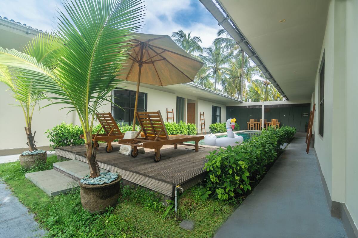 A covered outdoor area with a pool, lounge chairs, and a wooden deck.