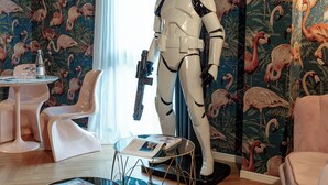 Een kamer met tropische behang, een Stormtrooper figuur, een ronde tafel en een bank.