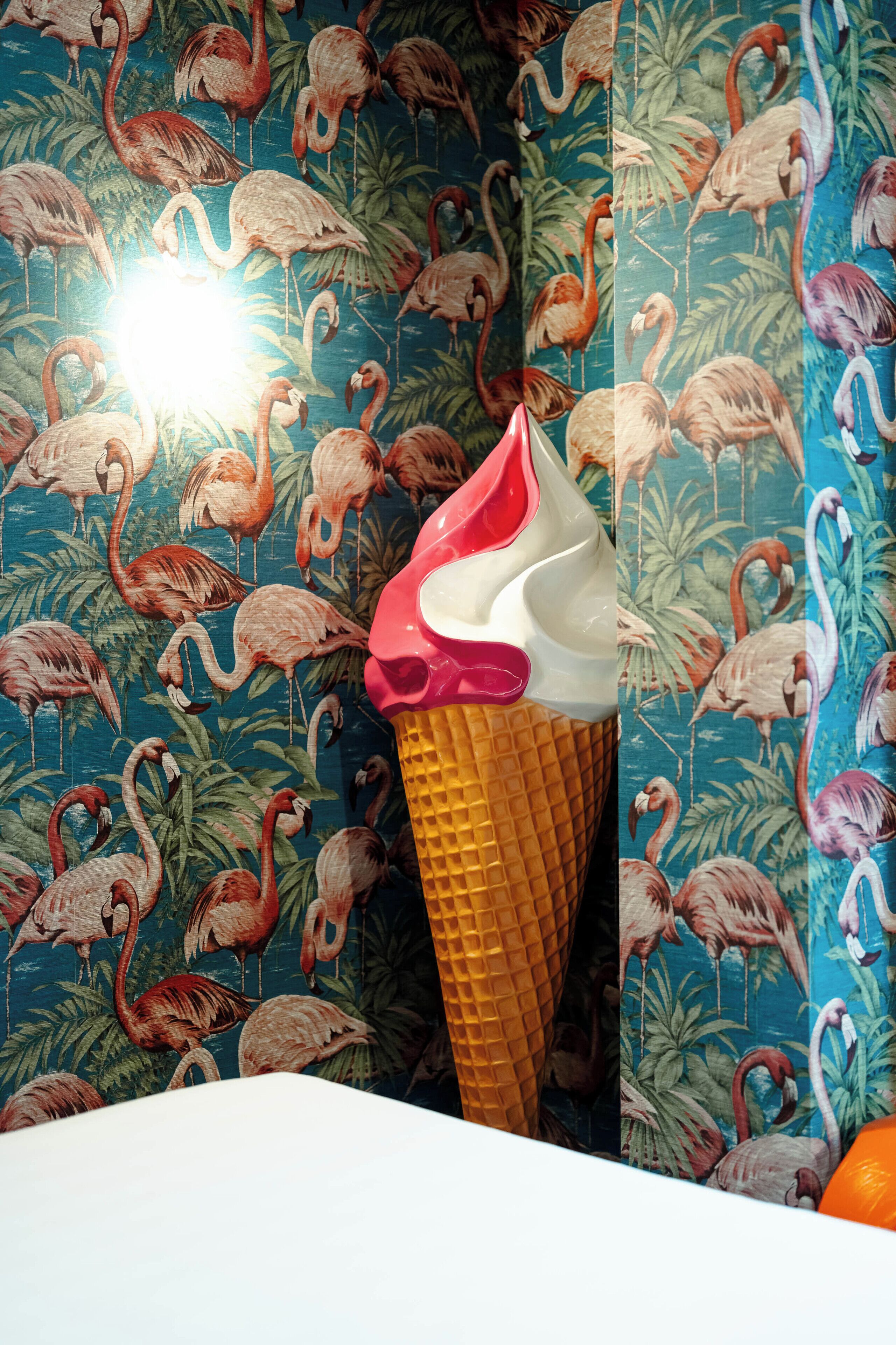 A wall with a flamingo pattern and a waffle cone with a pink topping.