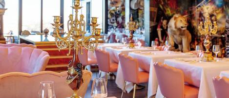 A restaurant with tables set for dining, featuring gold candelabras and pink chairs.