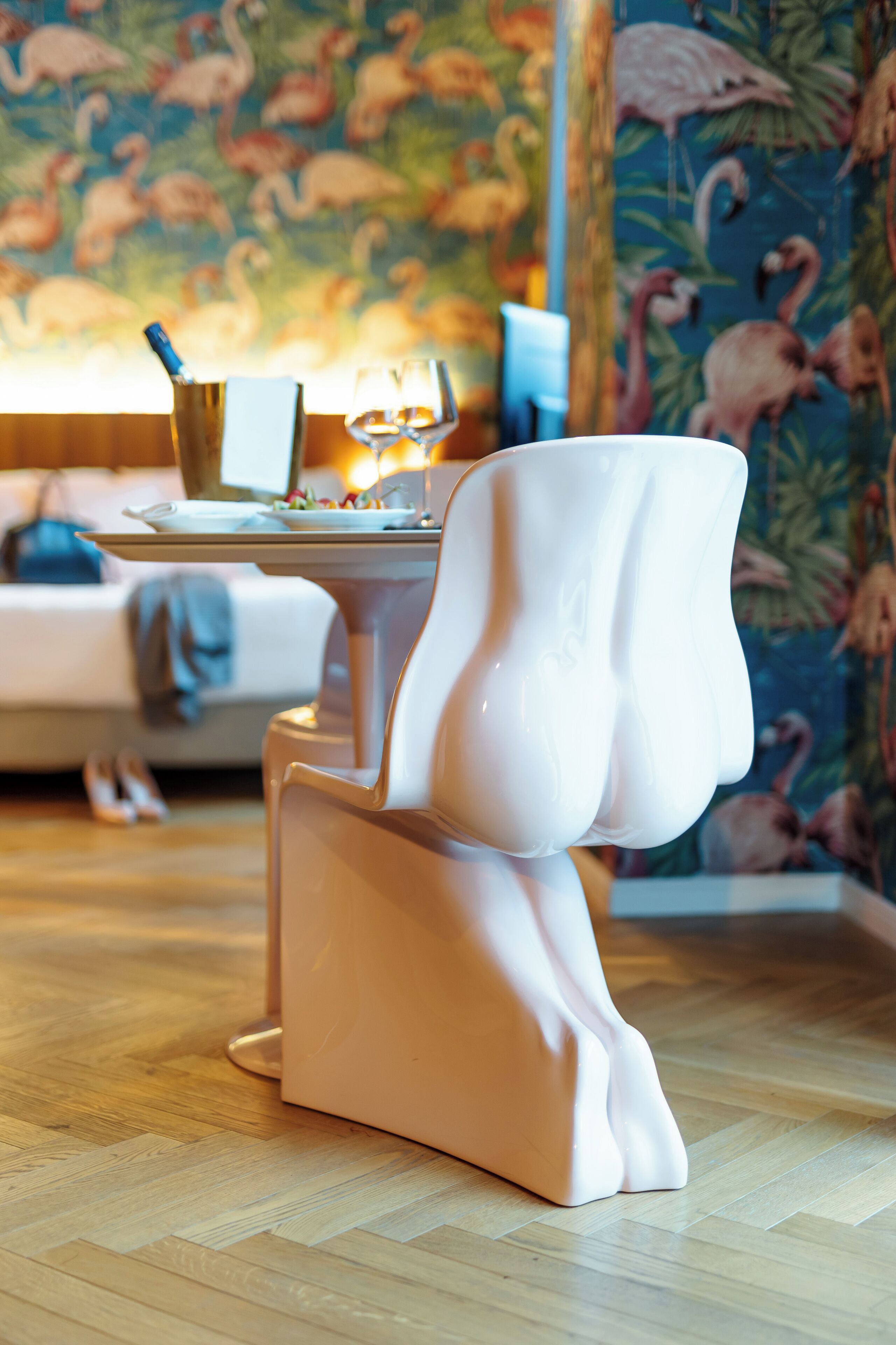 A modern dining area with a unique white chair design, a table with a glass of wine, and a floral wallpaper background.