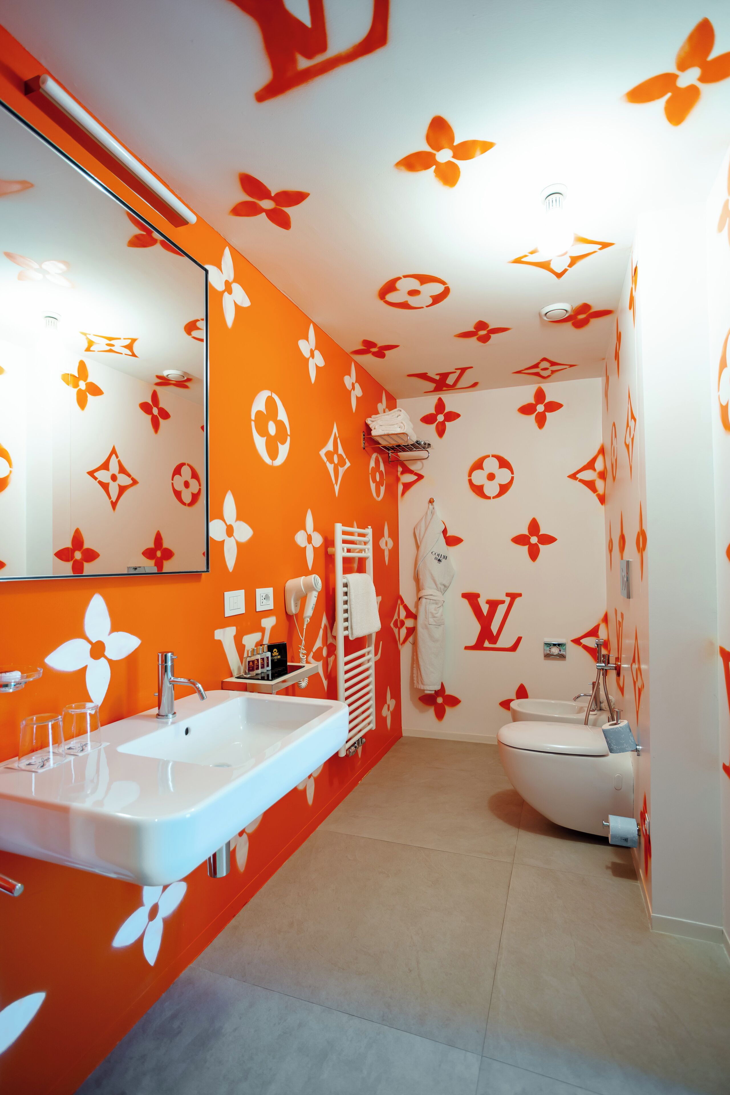 Ein Badezimmer mit einem weißen Waschbecken und WC, Wände in Orange mit floralem Muster und einem Spiegel über dem Waschbecken.