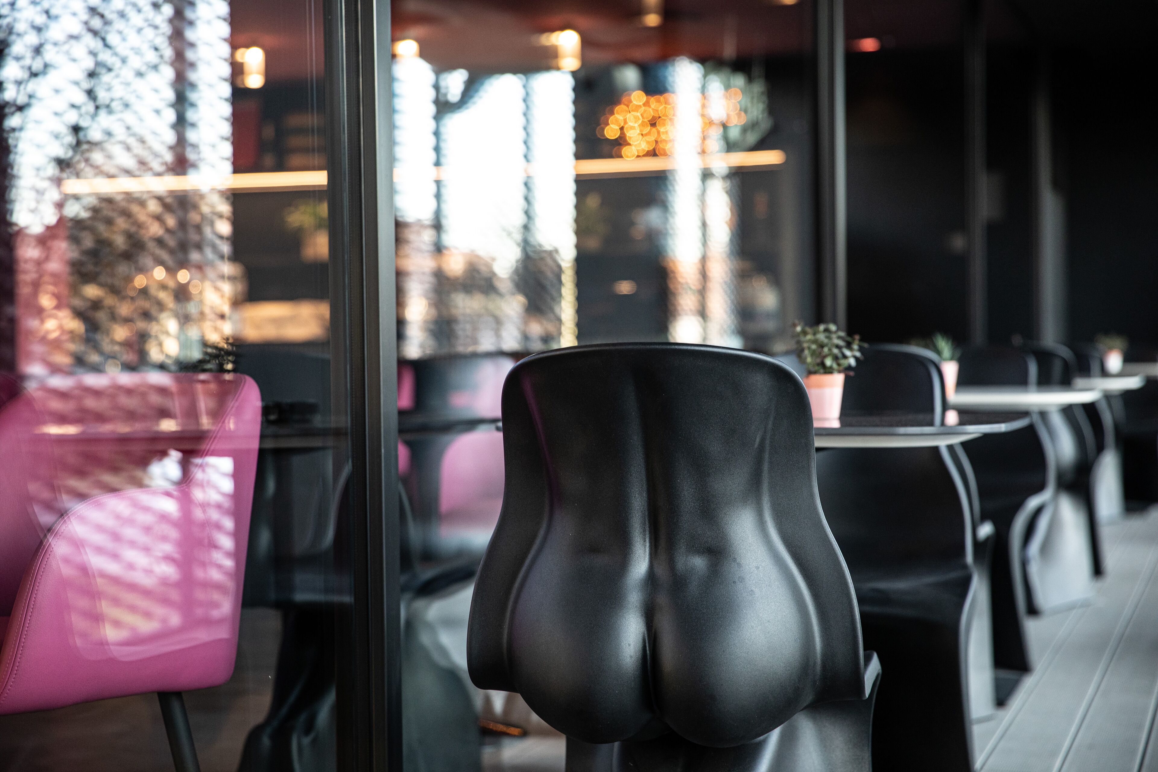 A restaurant interior with black and pink chairs, a glass partition, and a view of the city through the window.