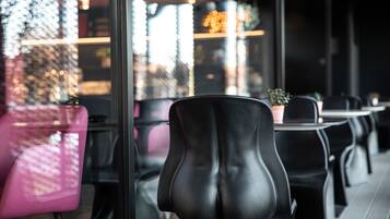 A restaurant interior with black and pink chairs, a glass partition, and a view of the city through the window.