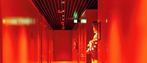Un couloir dont le plafond et les murs sont illuminés d’une lumière rouge, et qui mène à une porte au bout.