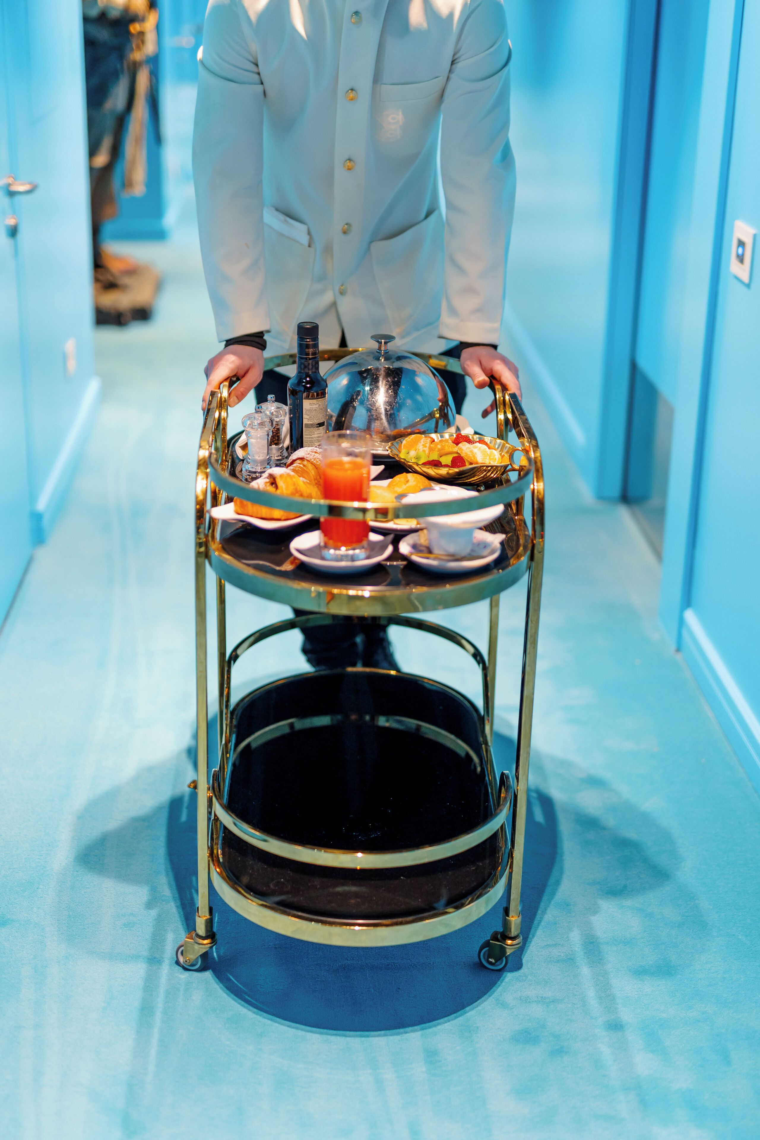 Une personne vêtue d’une chemise blanche pousse un chariot doré rempli de produits pour le petit-déjeuner.