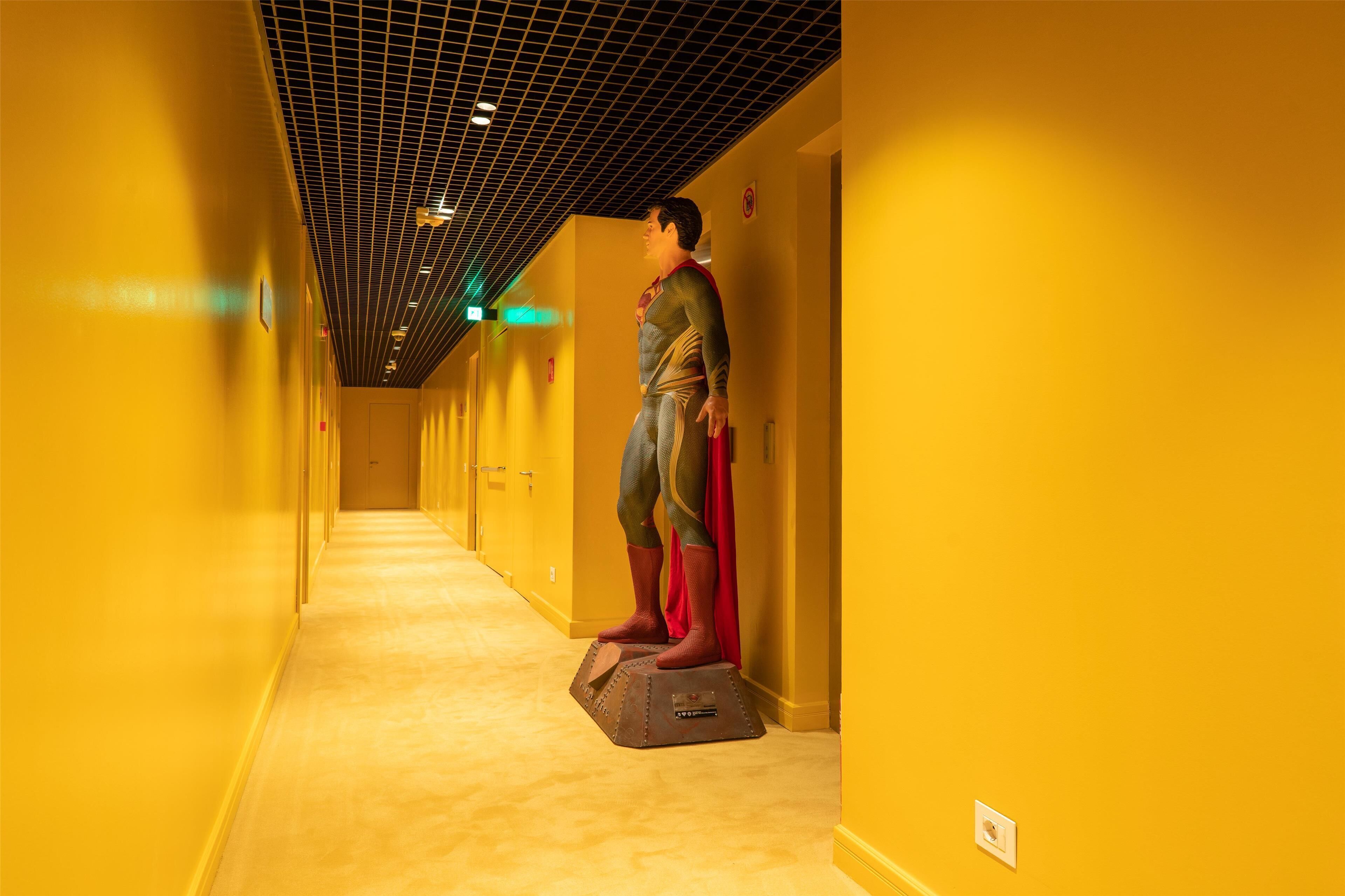 A person standing in a hallway with yellow walls and a grid ceiling.