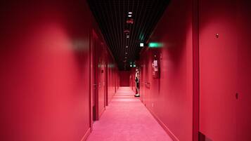A long, narrow corridor with red walls and a red carpet, leading to a door at the end.