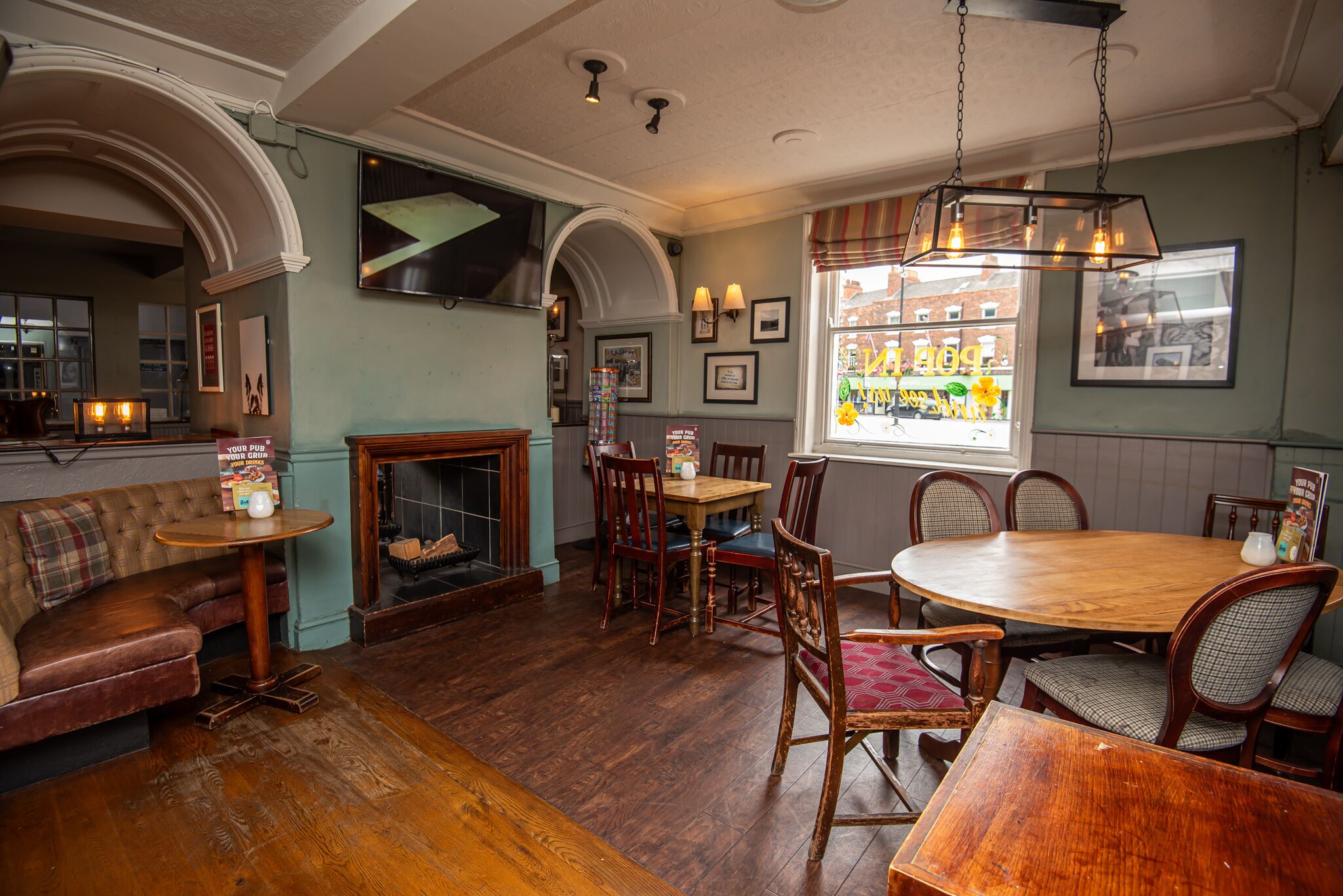 A cozy dining area with a round wooden table, cushioned chairs, a fireplace, and framed pictures on the walls.