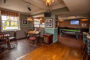 A billiards room with a pool table, wooden chairs, a table with a coffee cup, and a window with a view of the street. - The George Inn (Selby)