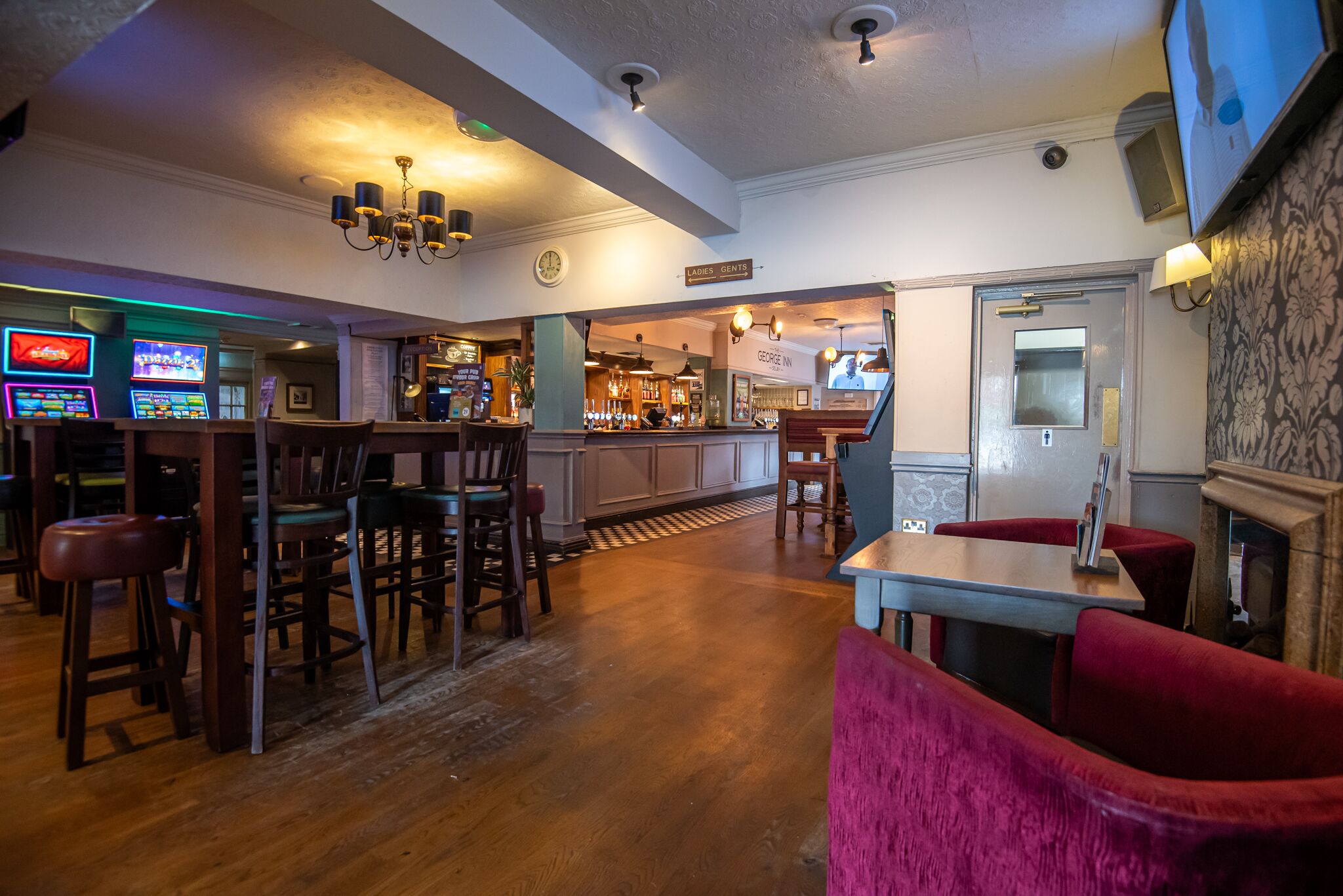 A bar area with wooden flooring, bar stools, and a television screen.