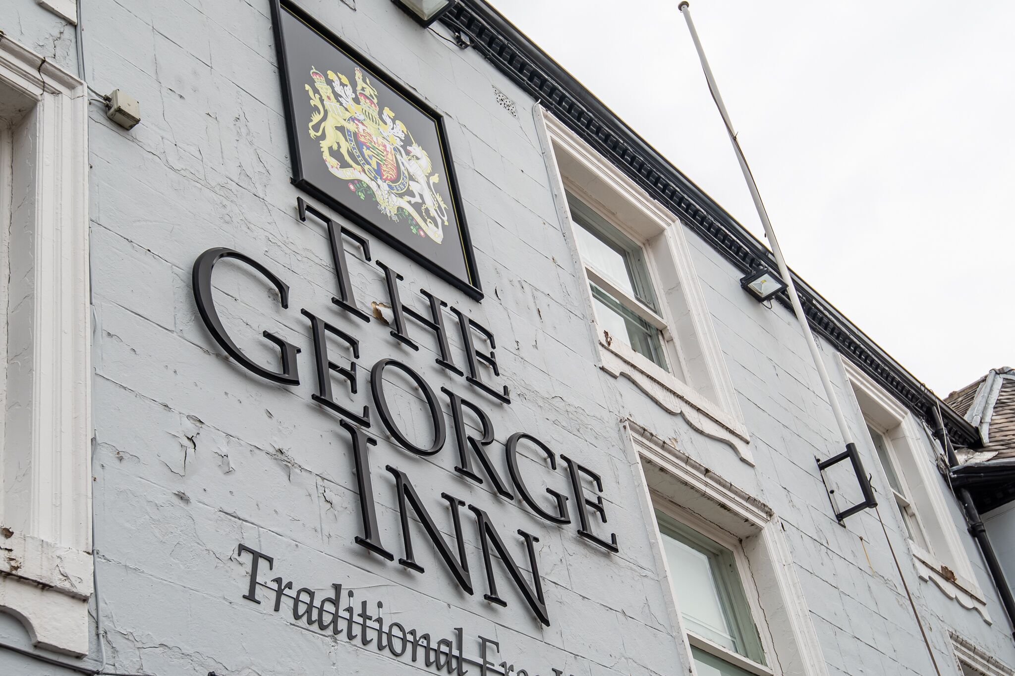 Een gebouw met een bord waarop 'The George Inn' staat en een familiewapen boven de naam.
