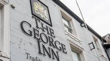 Een gebouw met een bord waarop 'The George Inn' staat en een familiewapen boven de naam.