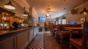 A bar area with a checkered floor, wooden bar counter, and seating area with wooden tables and chairs.