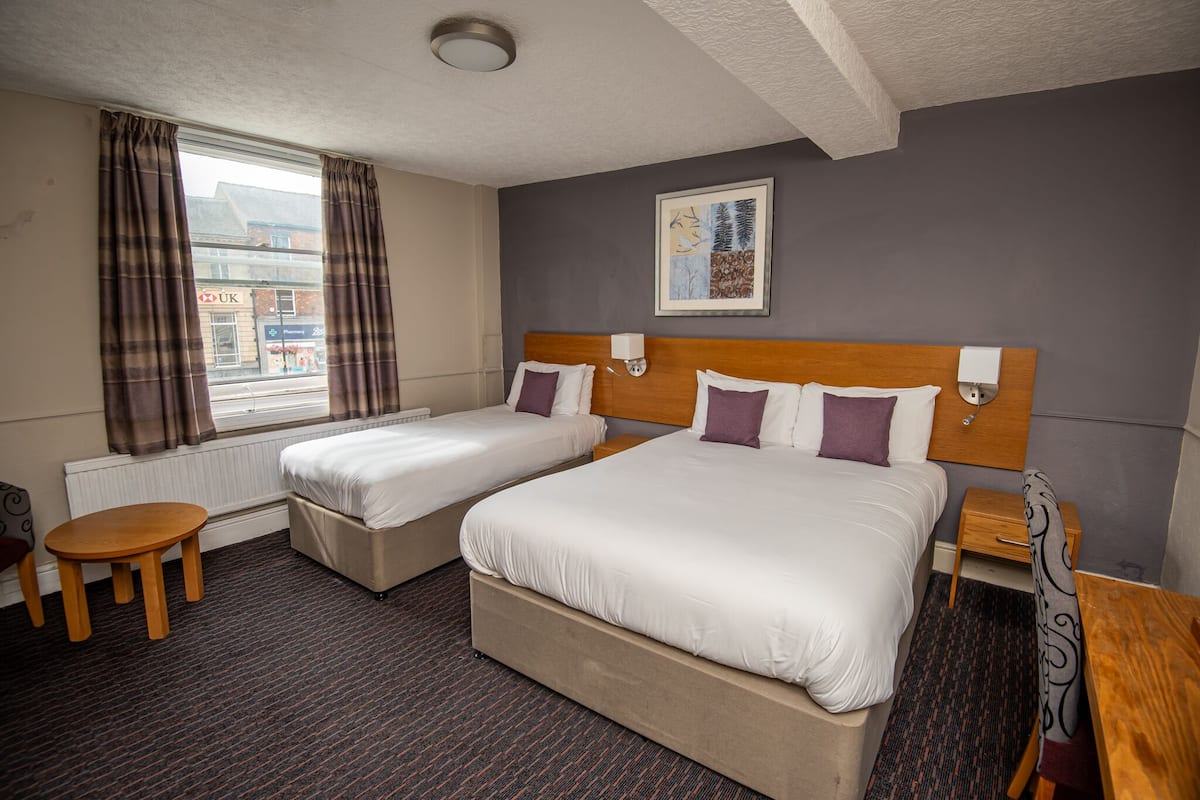 A hotel room with two beds, a small table, a chair, a nightstand, and a window with curtains.