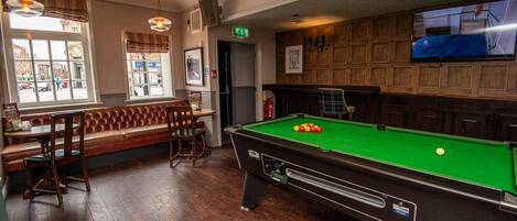 A billiards table with balls, a pool table, a bench, and a television mounted on the wall.