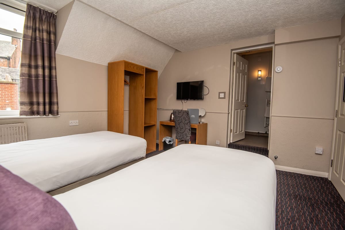 A hotel room with two beds, a wardrobe, a television, and a door leading to a bathroom.