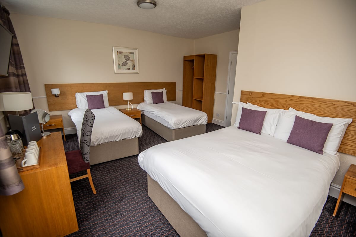 A hotel room with two beds, a desk with a lamp, a wardrobe, and a painting on the wall.