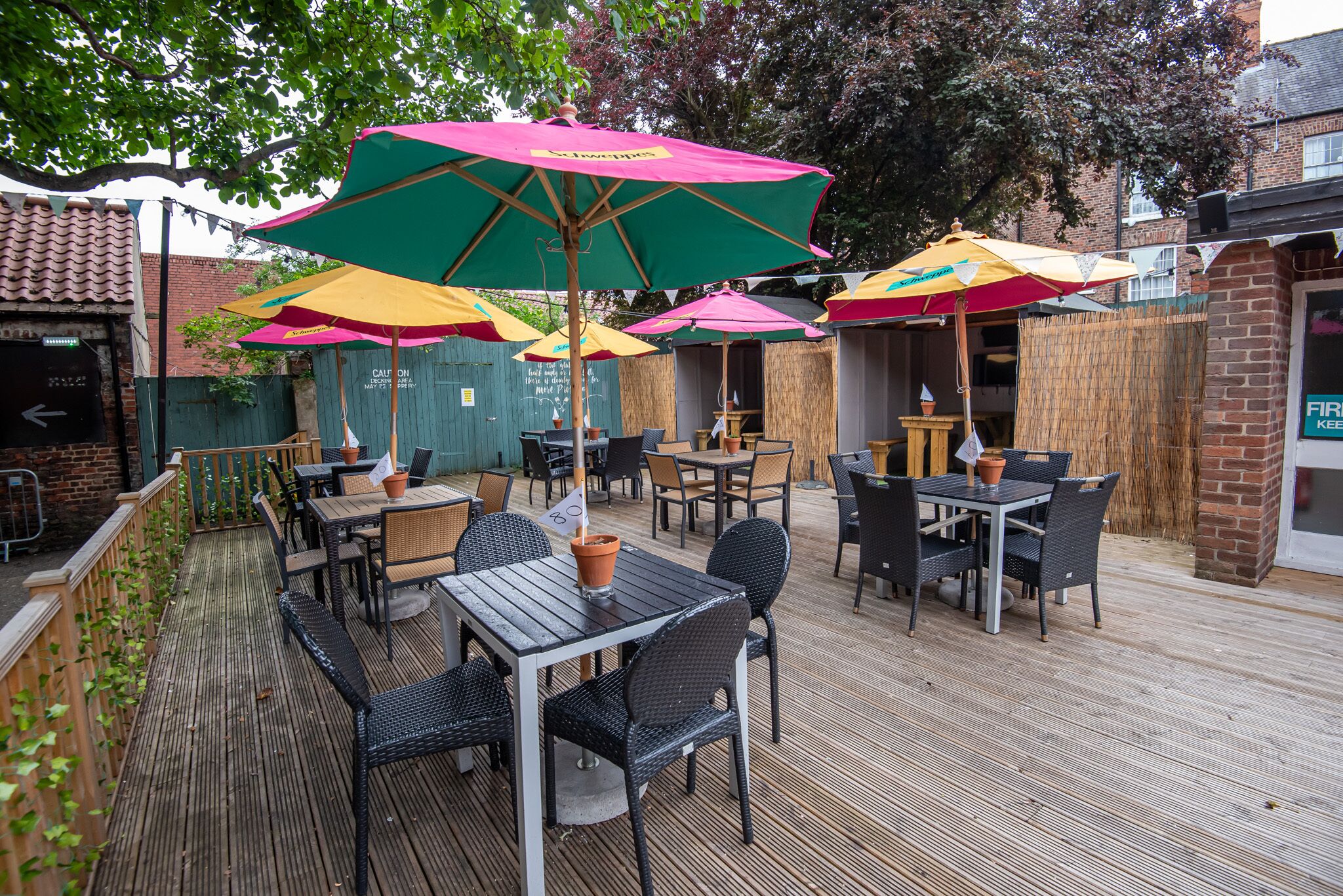 An outdoor patio area with tables and chairs, umbrellas, and a wooden deck.