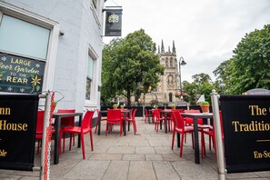 Un espace extérieur aménagé avec des chaises et des tables rouges, une grande enseigne indiquant un jardin à biÚre, et une vue sur un bùtiment historique en arriÚre-plan.