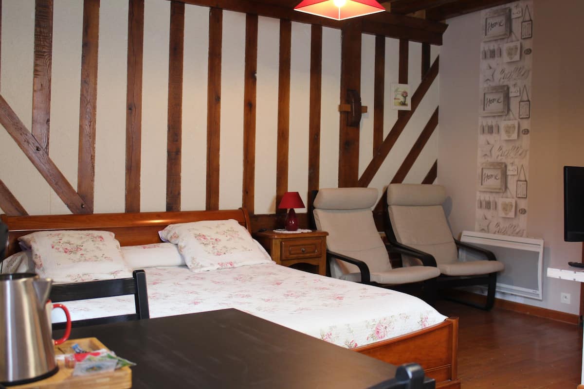 A bedroom with a wooden bed, a chair, a nightstand, and a wall with framed pictures.