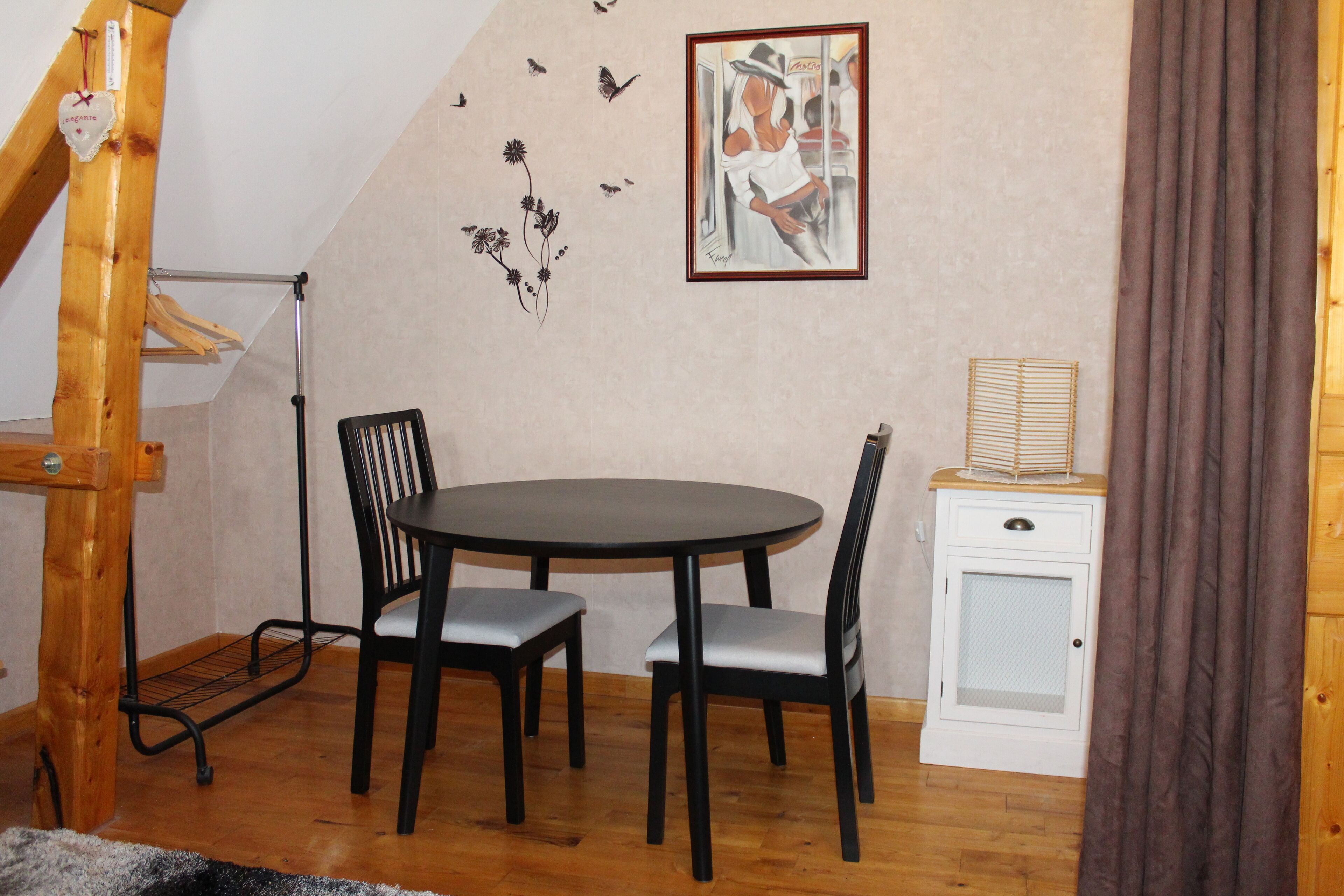 A dining area with a round table and four chairs, a small white cabinet, and a wall with a framed picture and decorative elements.