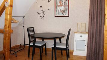 A dining area with a round table and four chairs, a small white cabinet, and a wall with a framed picture and decorative elements.