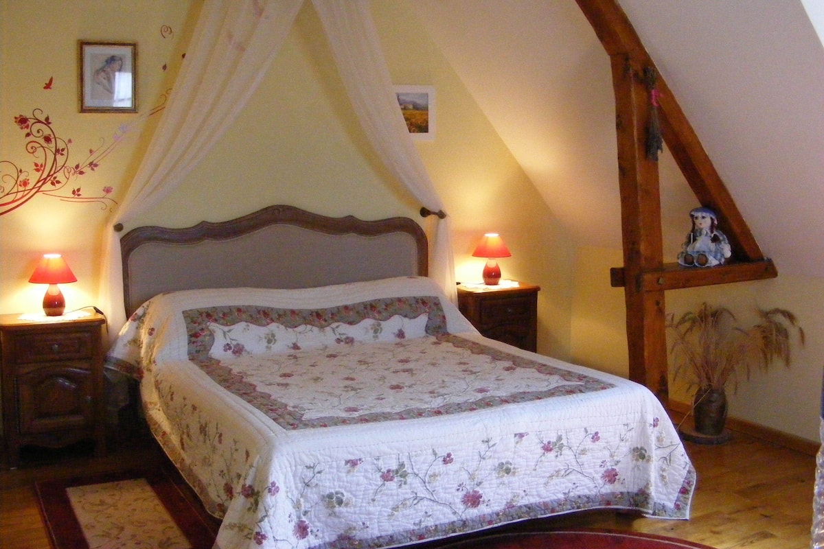 A bedroom with a four-poster bed, floral bedding, two bedside lamps, a picture on the wall, and a wooden beam structure.