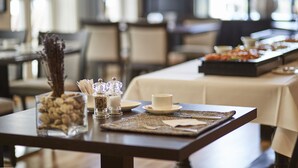 Una mesa de comedor con una taza, saleros, pimenteros y un recipiente de vidrio con frutos secos.