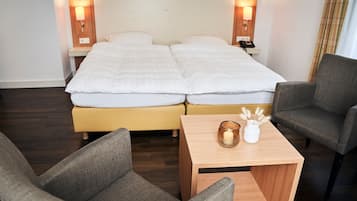 A hotel room with a double bed, bedside lamps, a small table with a candle and decorative items, and two armchairs.
