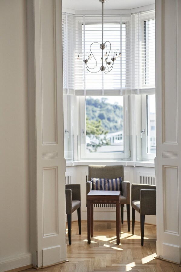 A bay window with white shutters, a wooden table, two chairs, and a chandelier.